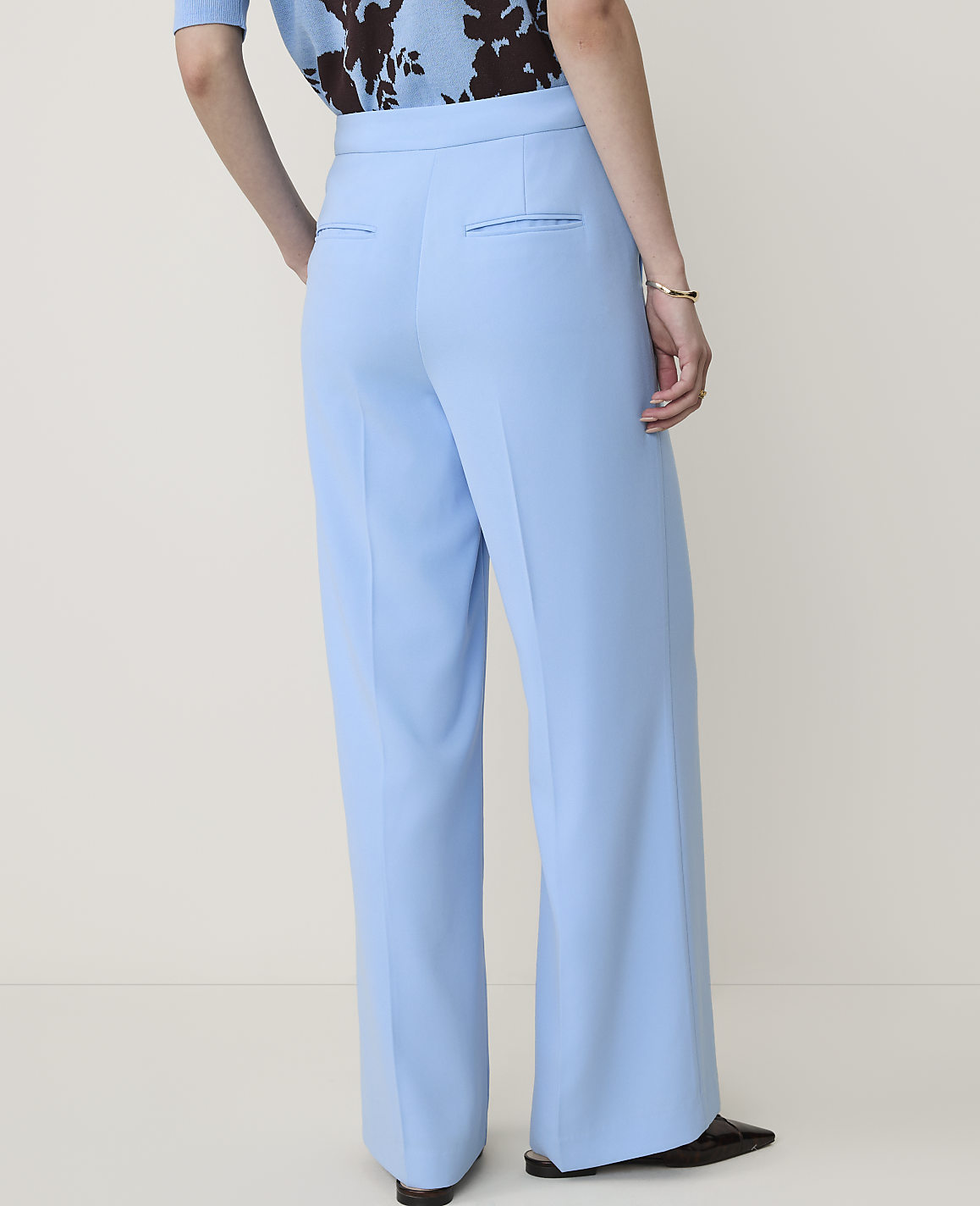A person wearing light blue wide-leg trousers and a patterned top stands against a plain, light-colored background.