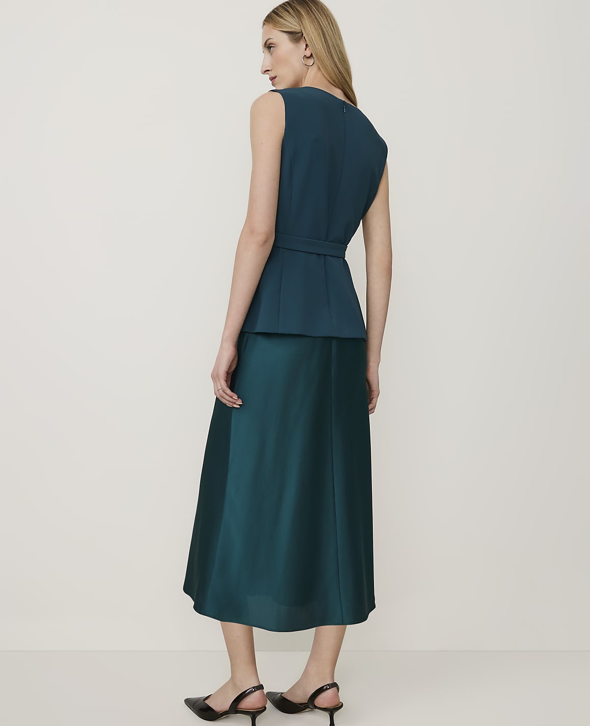 A woman in a teal peplum top and matching skirt stands against a plain, light background.