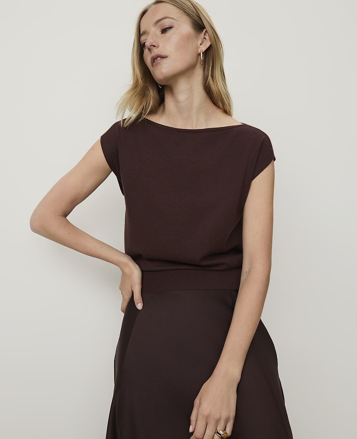 A woman in a brown top and skirt stands against a plain white background.