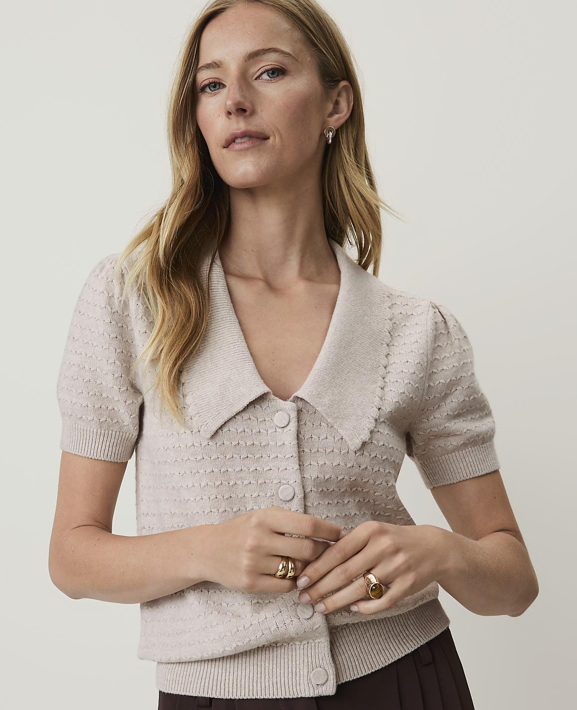 A woman in a beige cardigan with a Peter Pan collar stands against a plain, light background.
