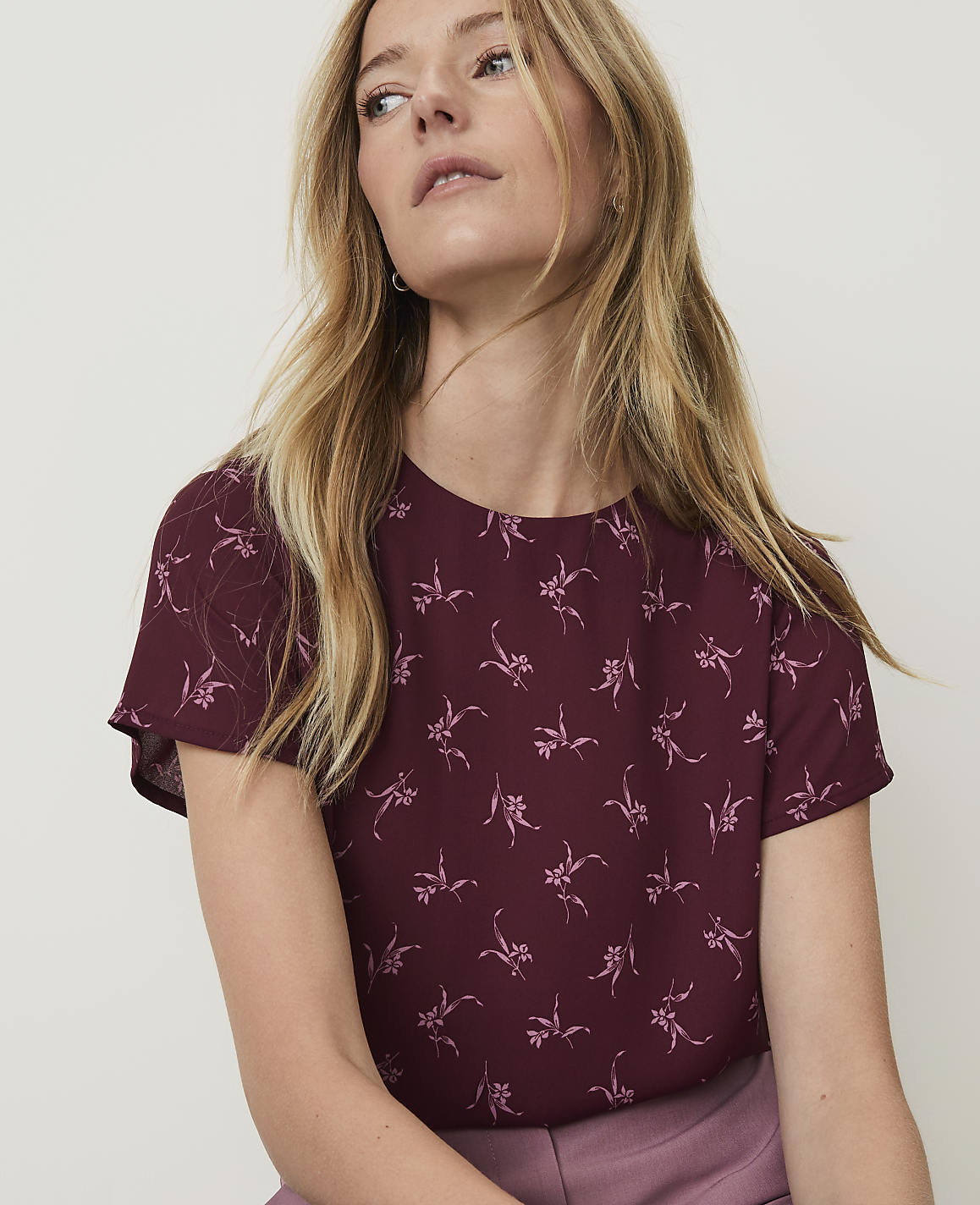 A woman with blonde hair wearing a maroon floral top is shown against a plain background.