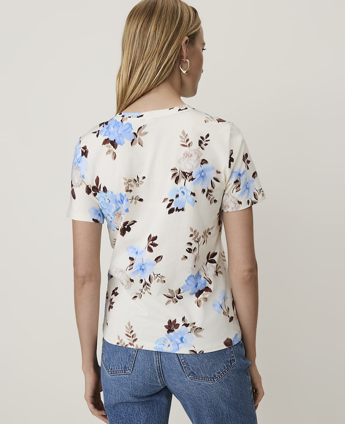 A woman in a floral t-shirt and jeans stands against a plain white background.