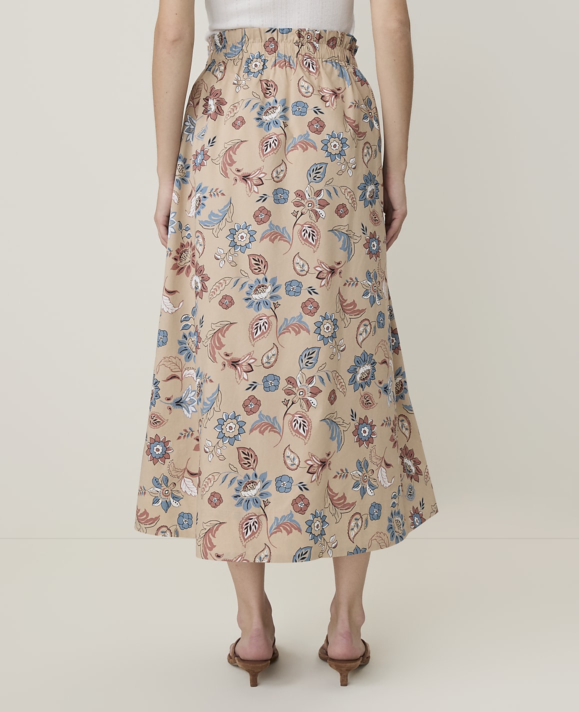 A person wearing a floral print skirt stands against a plain, light-colored background.