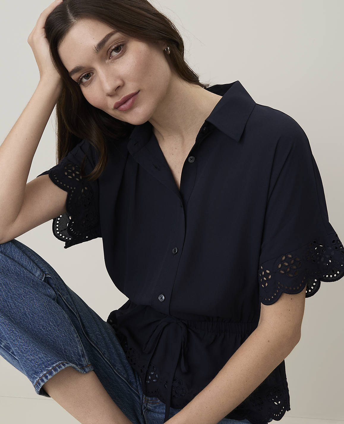 A woman in a navy blue shirt and jeans poses against a plain background.