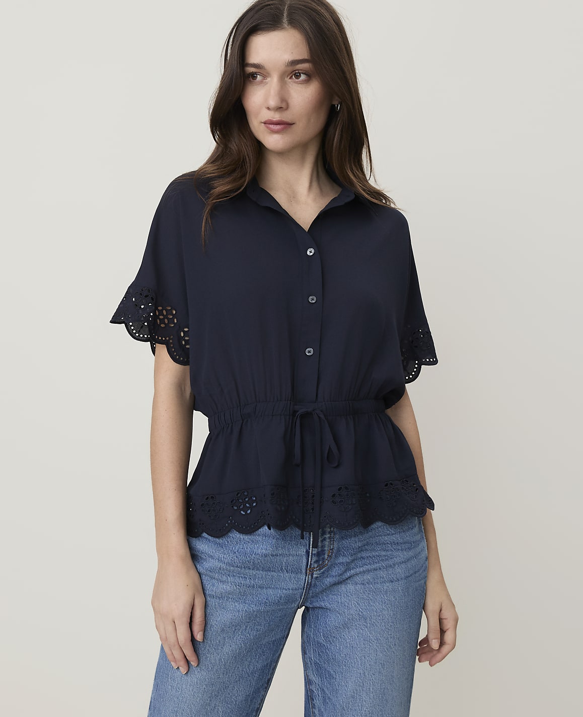 A woman in a navy blue blouse and jeans stands against a plain, light-colored background.