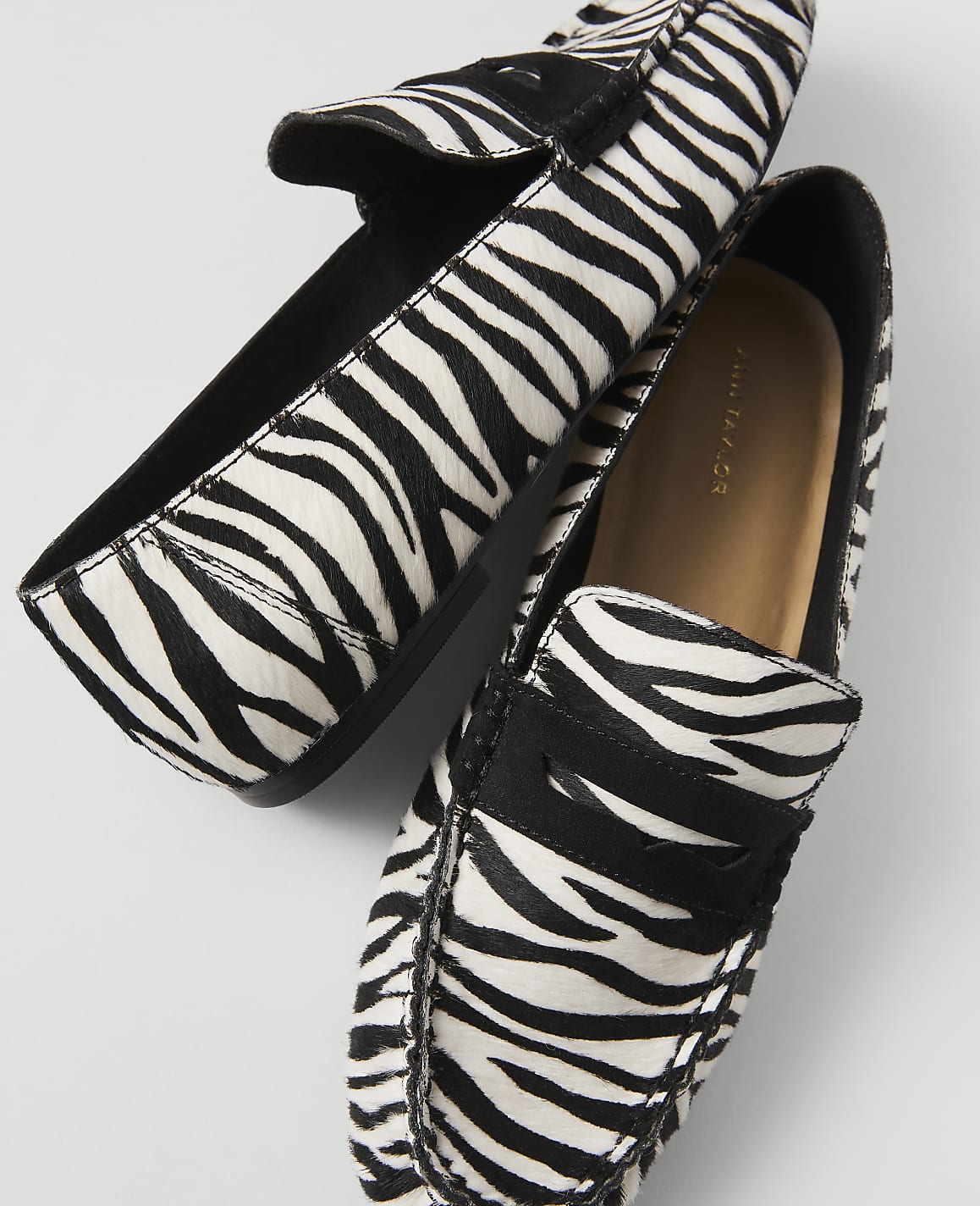 A pair of zebra-print loafers rests on a plain white background.