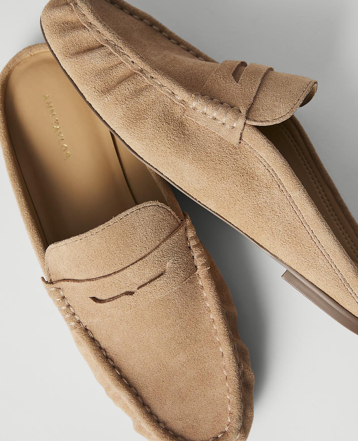 A pair of tan suede loafers with visible stitching rests on a plain white background.