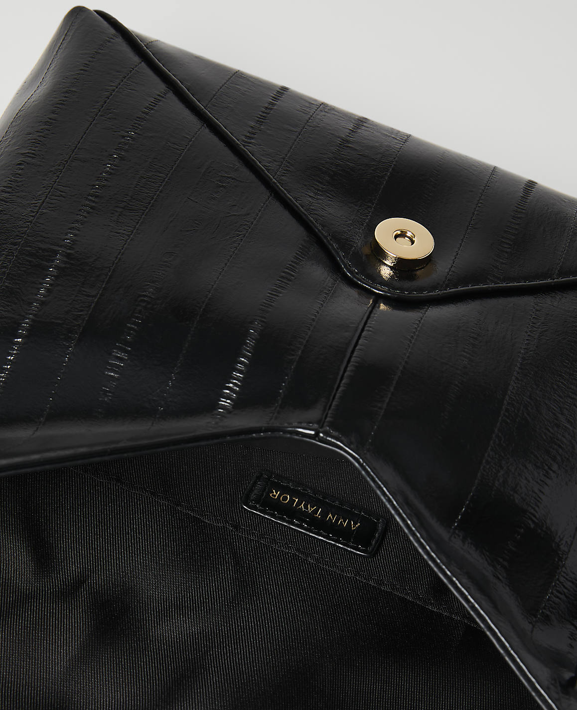 A glossy black clutch with a gold snap closure is laid open against a plain white background.