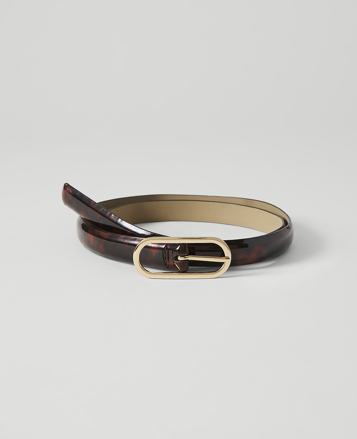 A glossy, tortoiseshell-patterned belt with a gold oval buckle lies coiled on a plain white background.