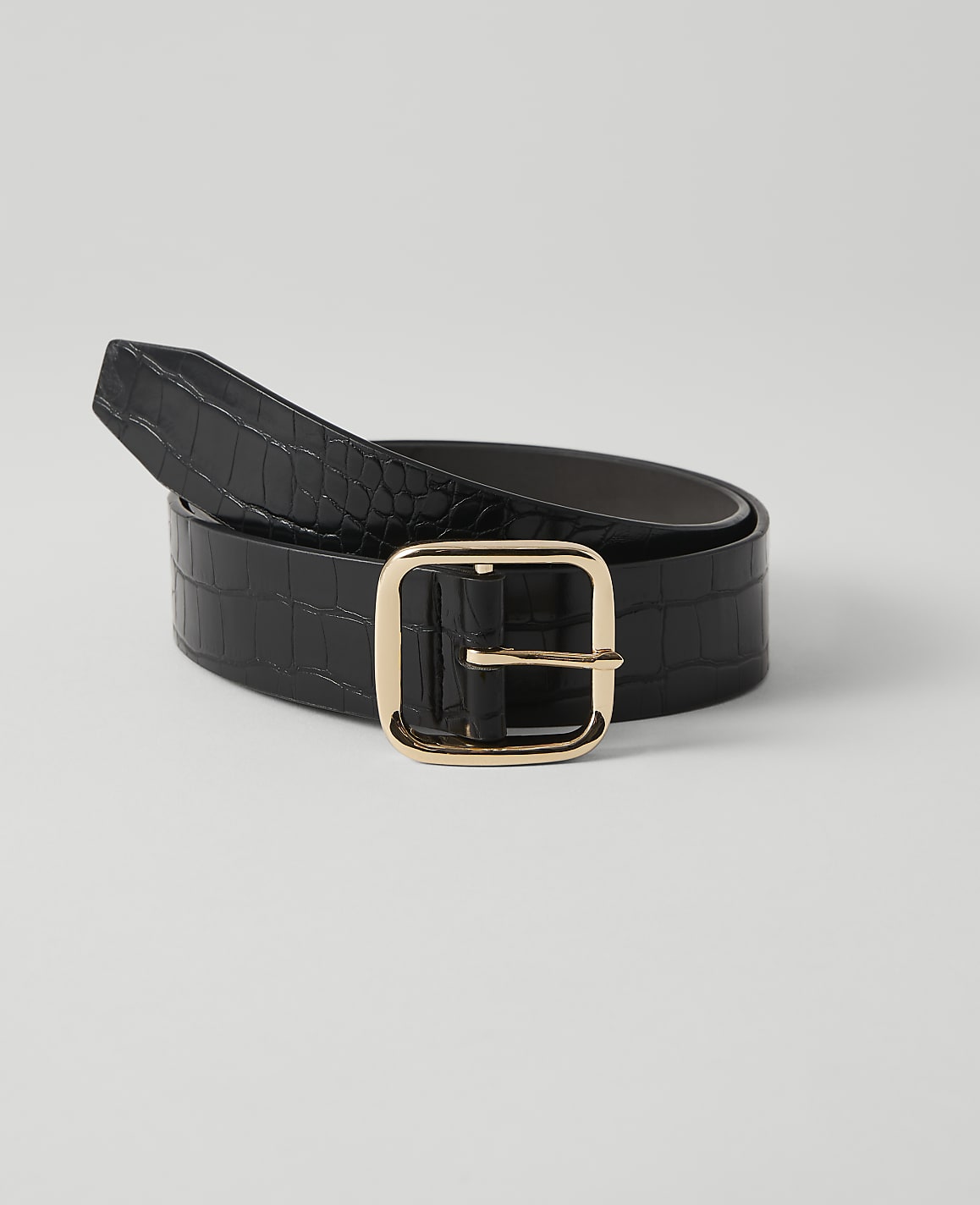 A black crocodile-embossed leather belt with a gold buckle rests on a plain white background.