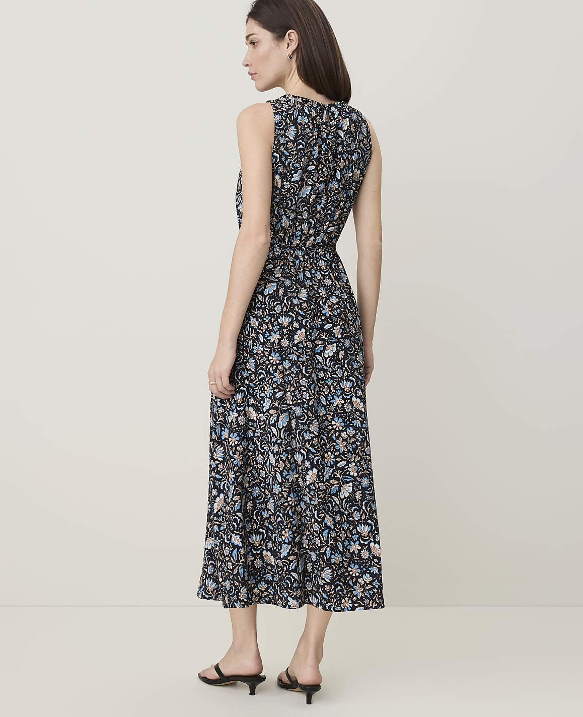 A woman in a floral print dress stands against a plain, light-colored background.