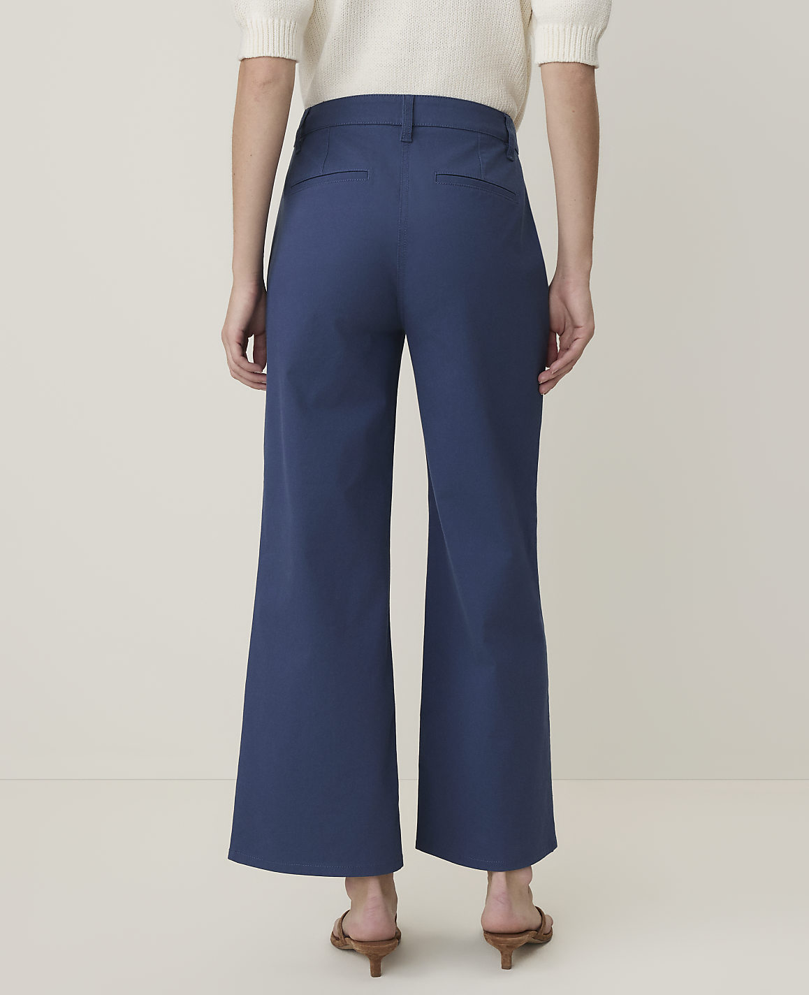 A person wearing blue wide-leg pants and brown heeled sandals stands against a plain, light-colored background.