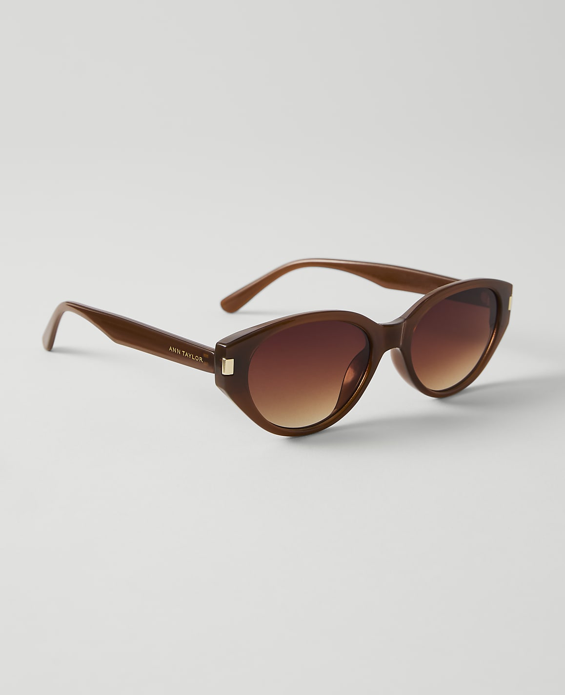 Brown cat-eye sunglasses with gradient lenses rest on a plain white background.