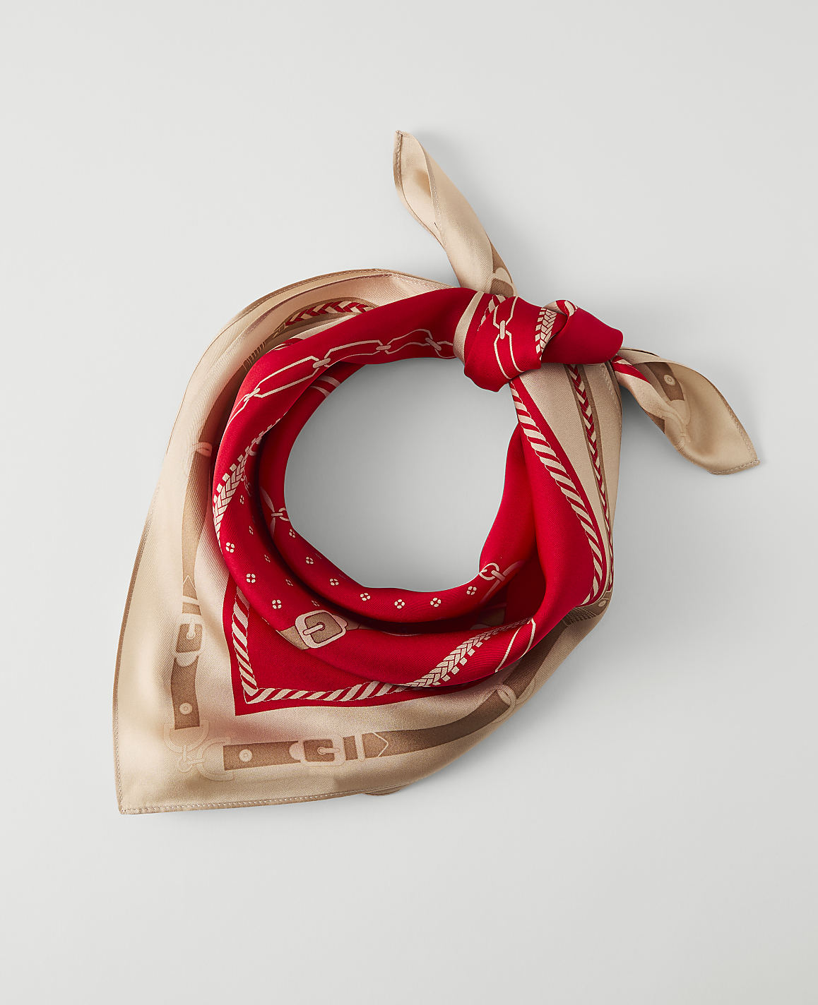 A red and tan patterned silk scarf is laid flat against a plain white background.