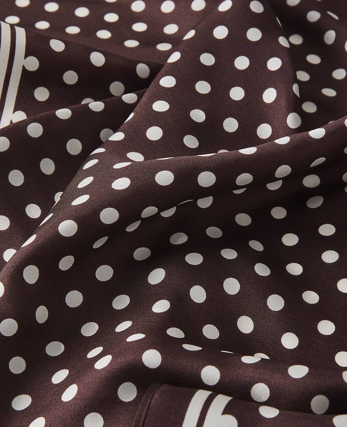 A close-up of a brown polka dot fabric with white dots fills the foreground, while the background is a continuation of the same patterned material.