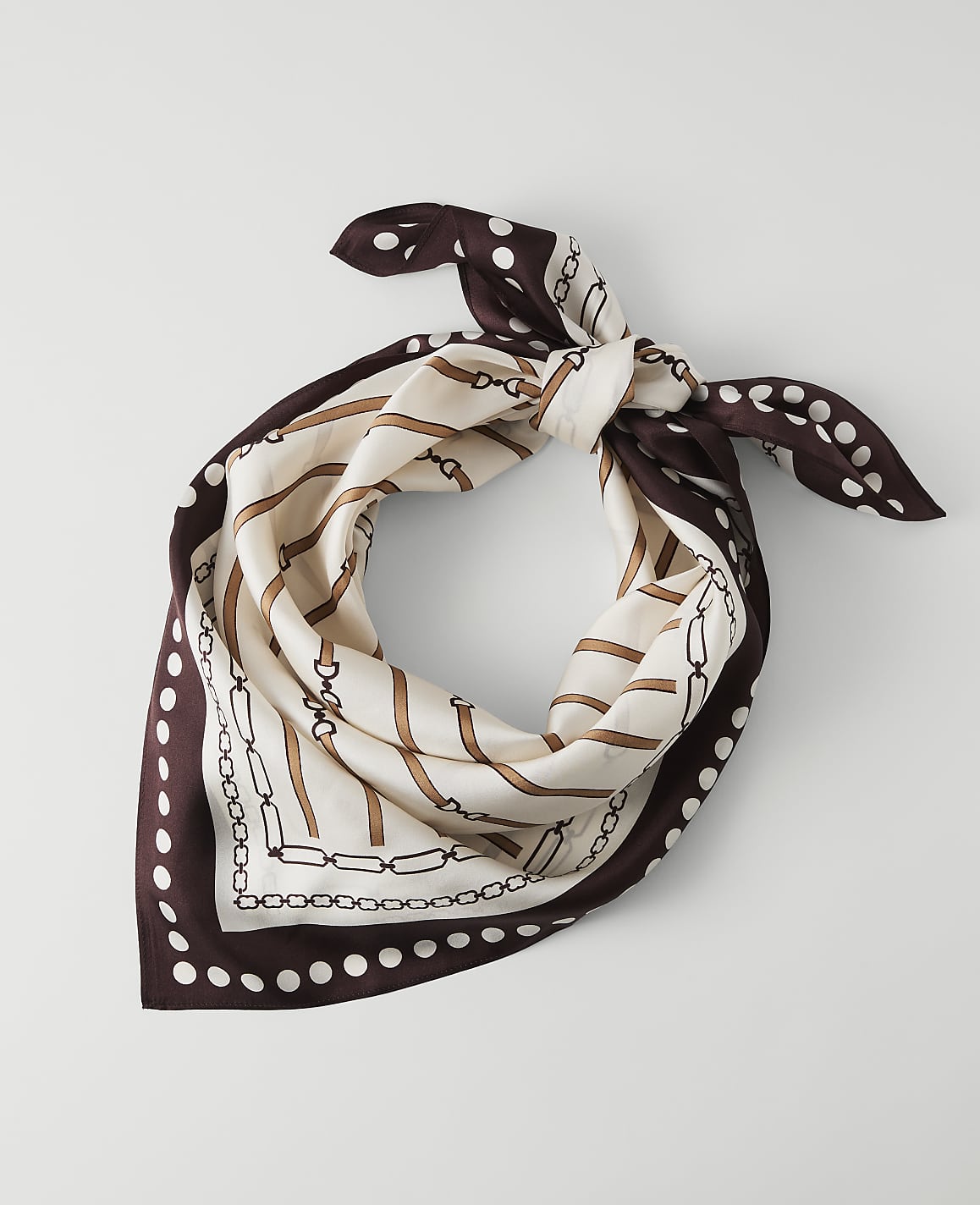 A silk scarf with a chain and polka dot pattern is laid out on a plain white background.