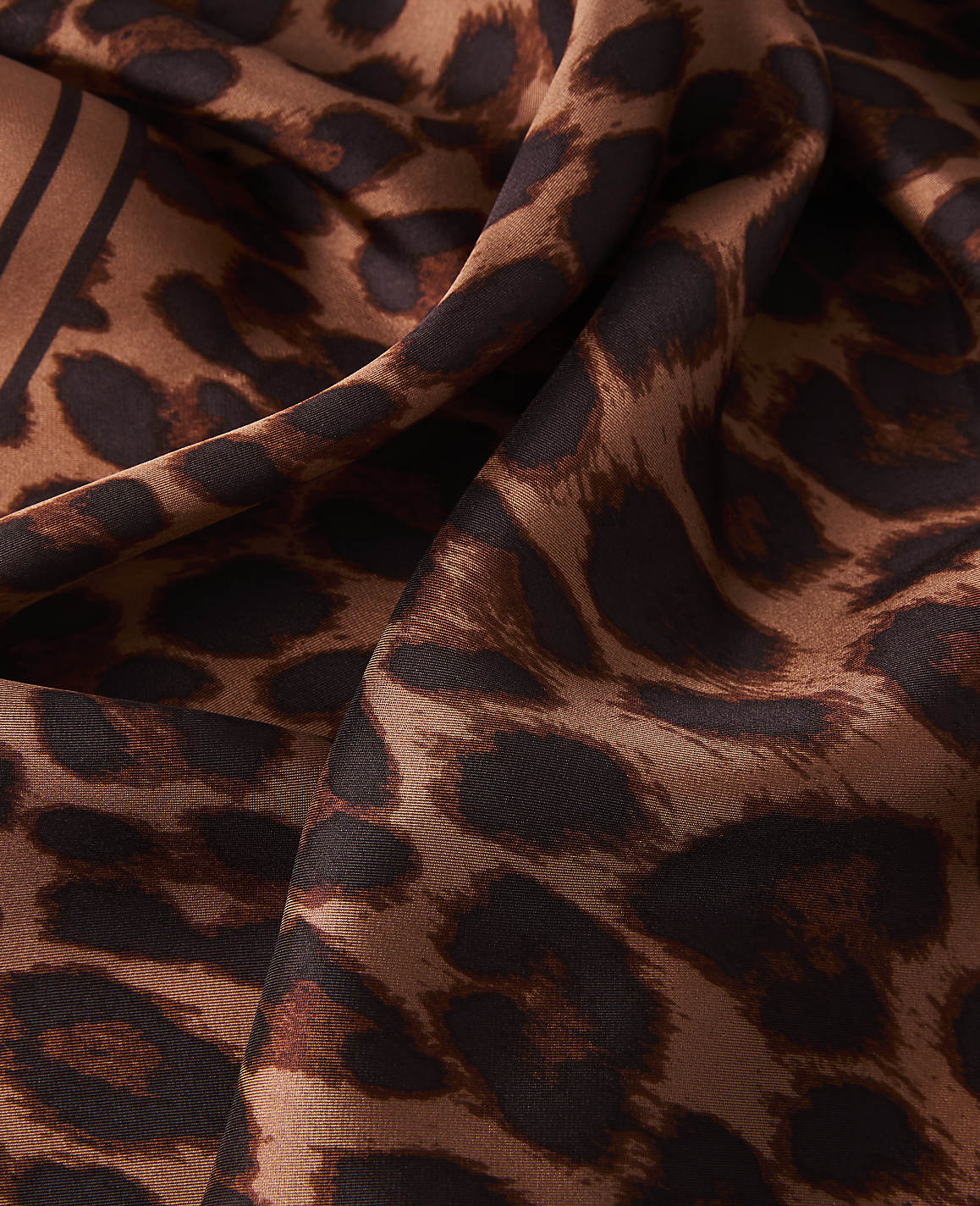 A close-up of a brown leopard print fabric with folds and shadows in the foreground, and a blurred continuation of the pattern in the background.