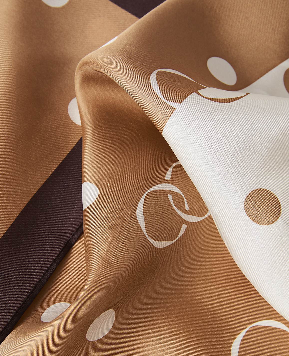 A close-up of a silky brown and white polka-dotted fabric with a dark brown stripe in the background.