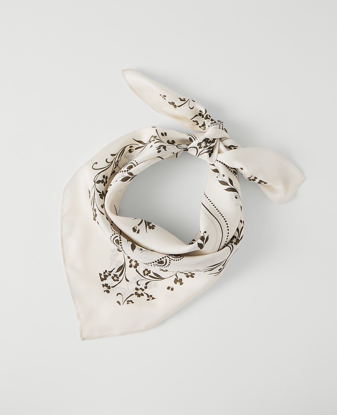 A cream-colored bandana with a dark floral pattern is tied in a knot against a plain white background.