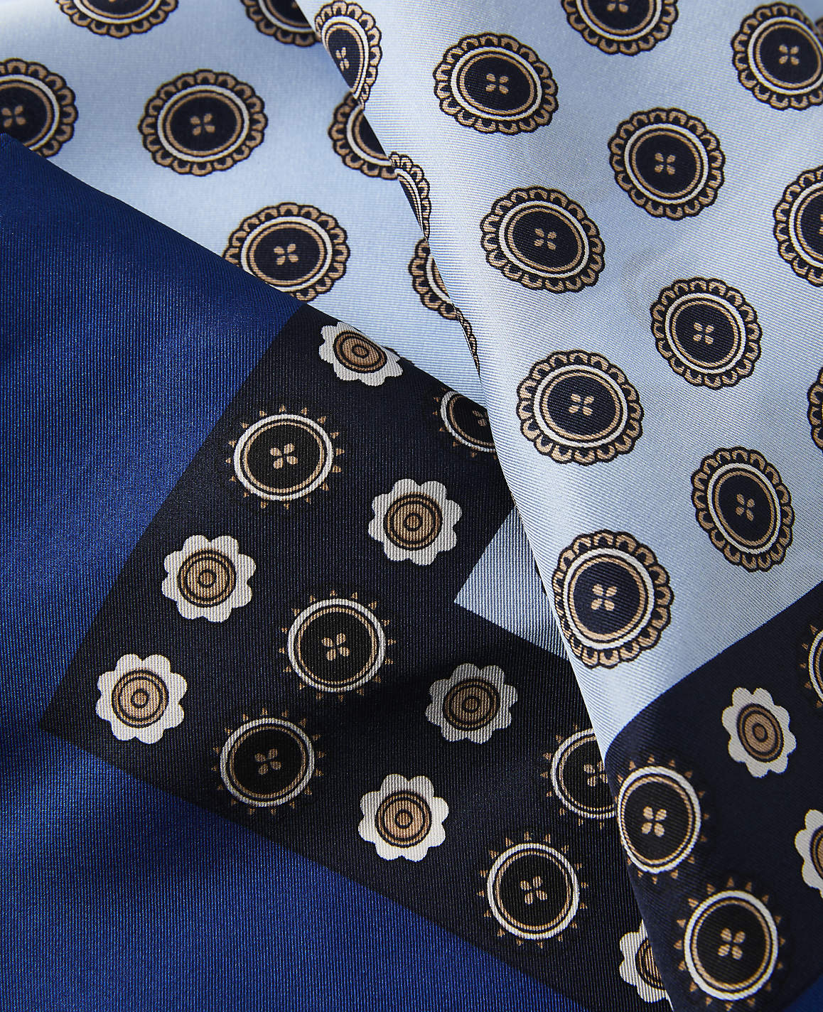 A close-up of a silk scarf with a geometric pattern of circular motifs in shades of blue and brown is laid out against a solid blue background.