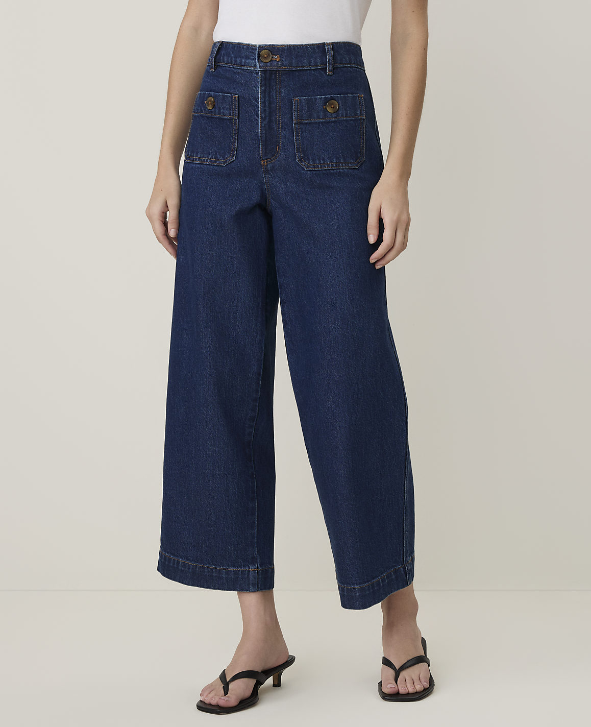 A person models wide-leg denim culottes with patch pockets and black heeled sandals against a plain, light-colored background.