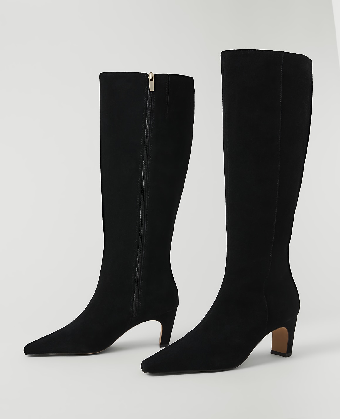 A pair of black suede knee-high boots with pointed toes and block heels stand on a white background.