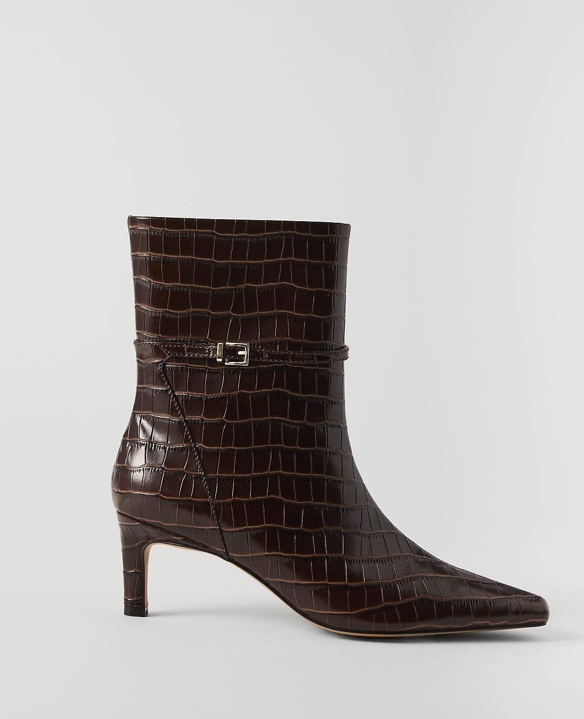 A brown, croc-embossed ankle boot with a gold buckle detail stands on a white background.