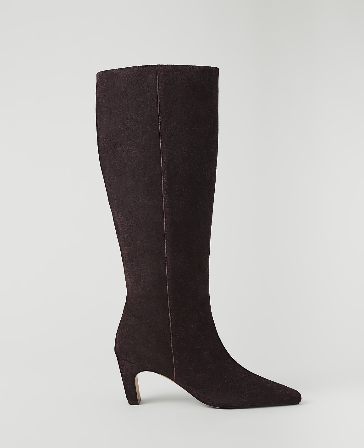 A dark brown suede knee-high boot with a pointed toe and a curved heel stands against a plain, light gray background.