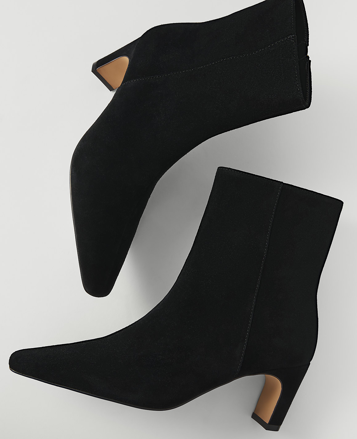 Two black suede ankle boots with pointed toes and block heels are arranged on a plain white background.