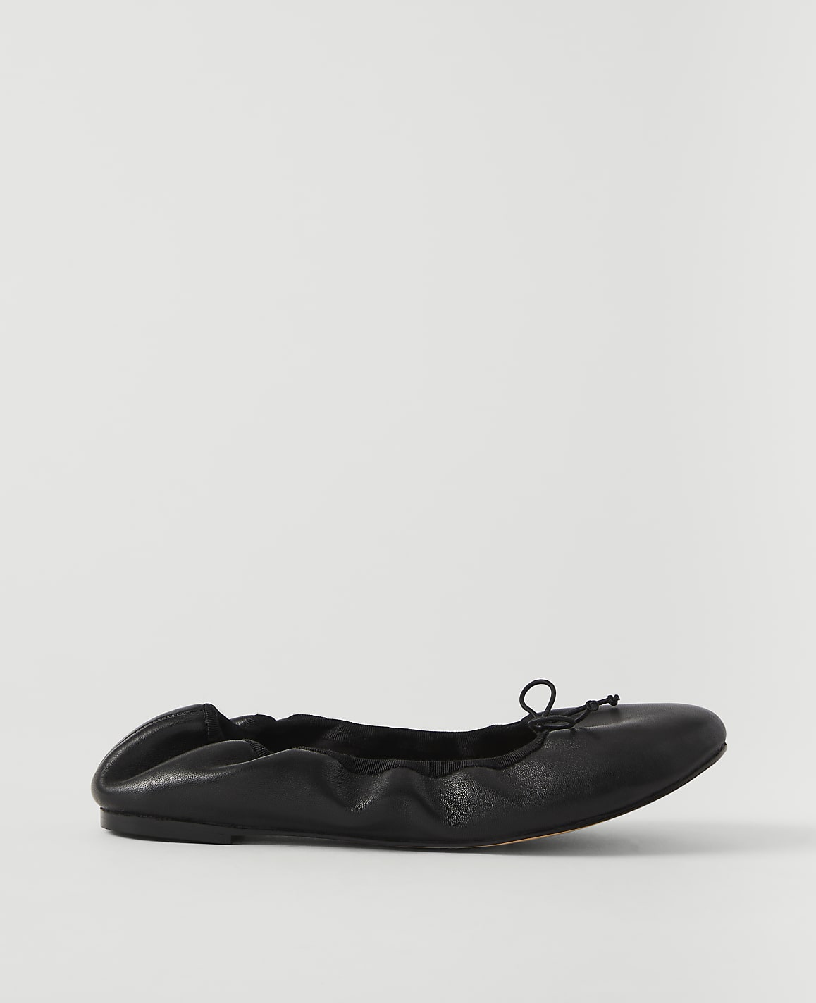 A black leather ballet flat with a drawstring bow rests on a plain white background.