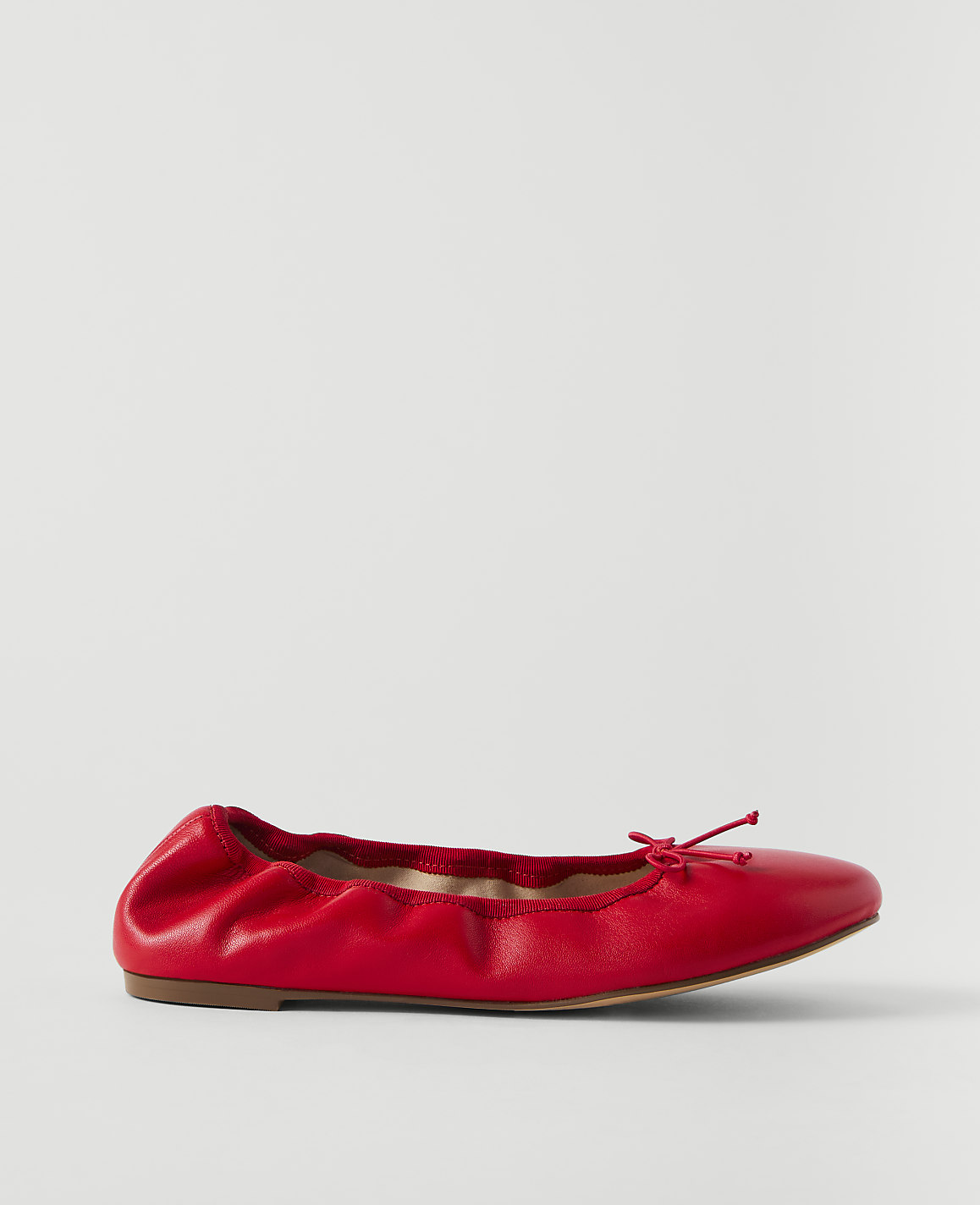 A red leather ballet flat with a bow sits on a plain white background.
