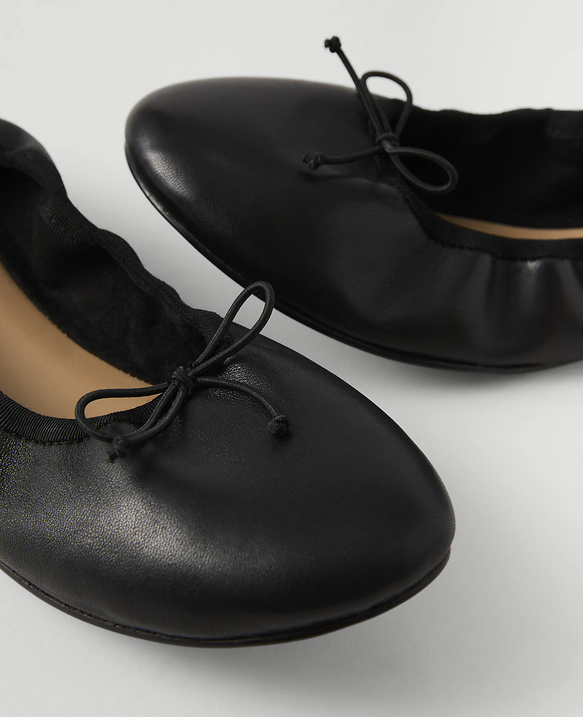 Two black ballet flats with small bows are in the foreground against a plain white background.