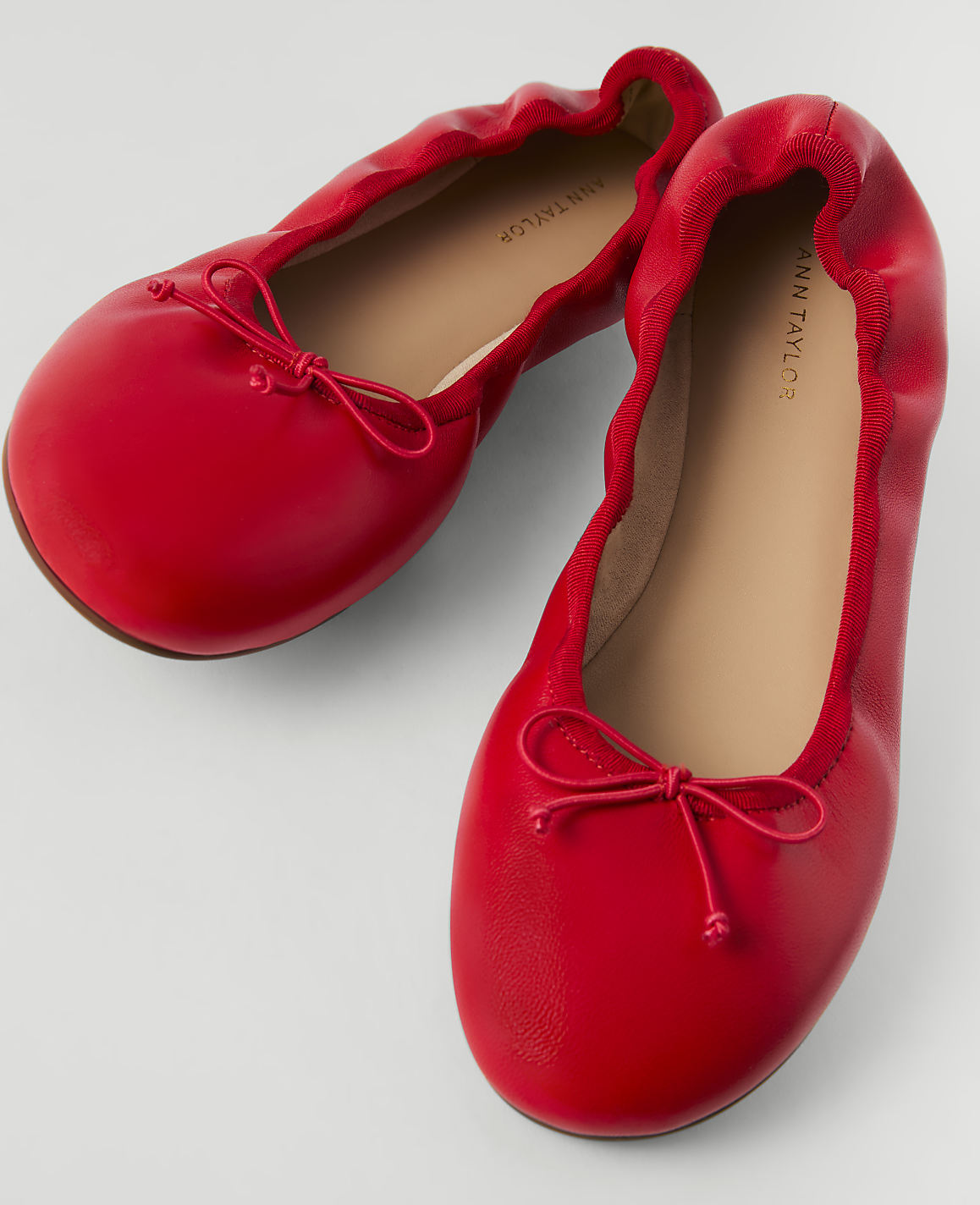 A pair of bright red ballet flats with small bows are displayed on a plain white background.
