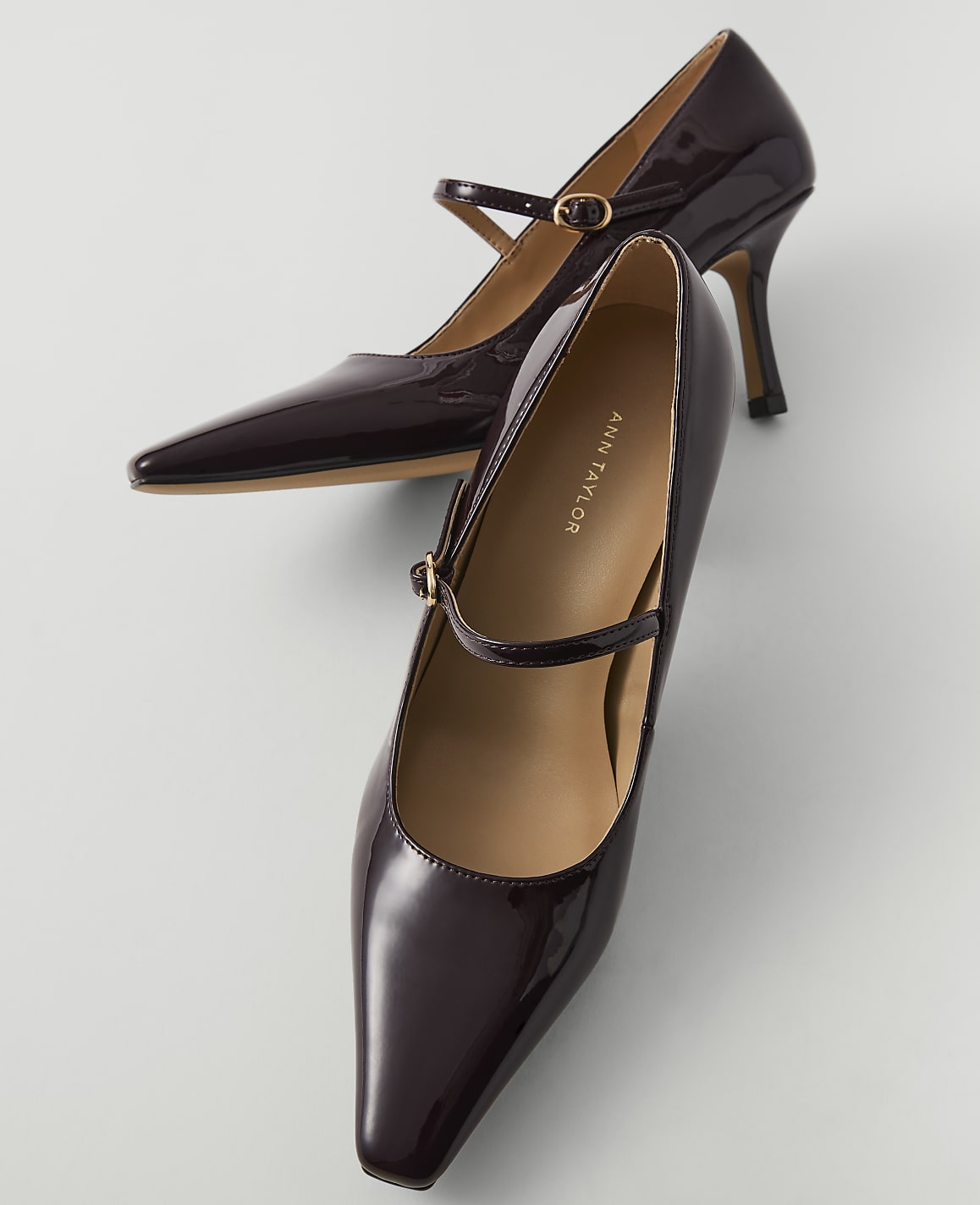 A pair of glossy burgundy Mary Jane heels with pointed toes rests on a light gray surface.