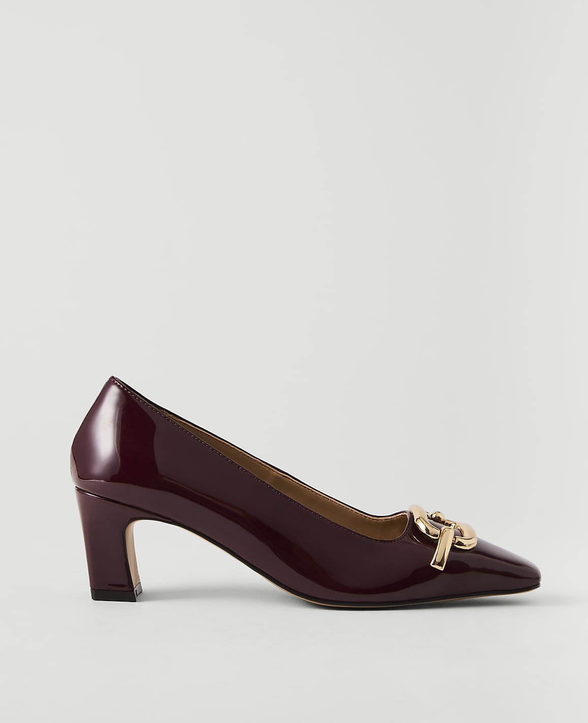 A glossy burgundy pump with a gold buckle sits on a plain white background.