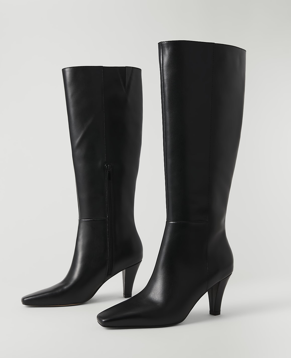 A pair of black leather knee-high boots with pointed toes and stiletto heels stand against a plain white background.