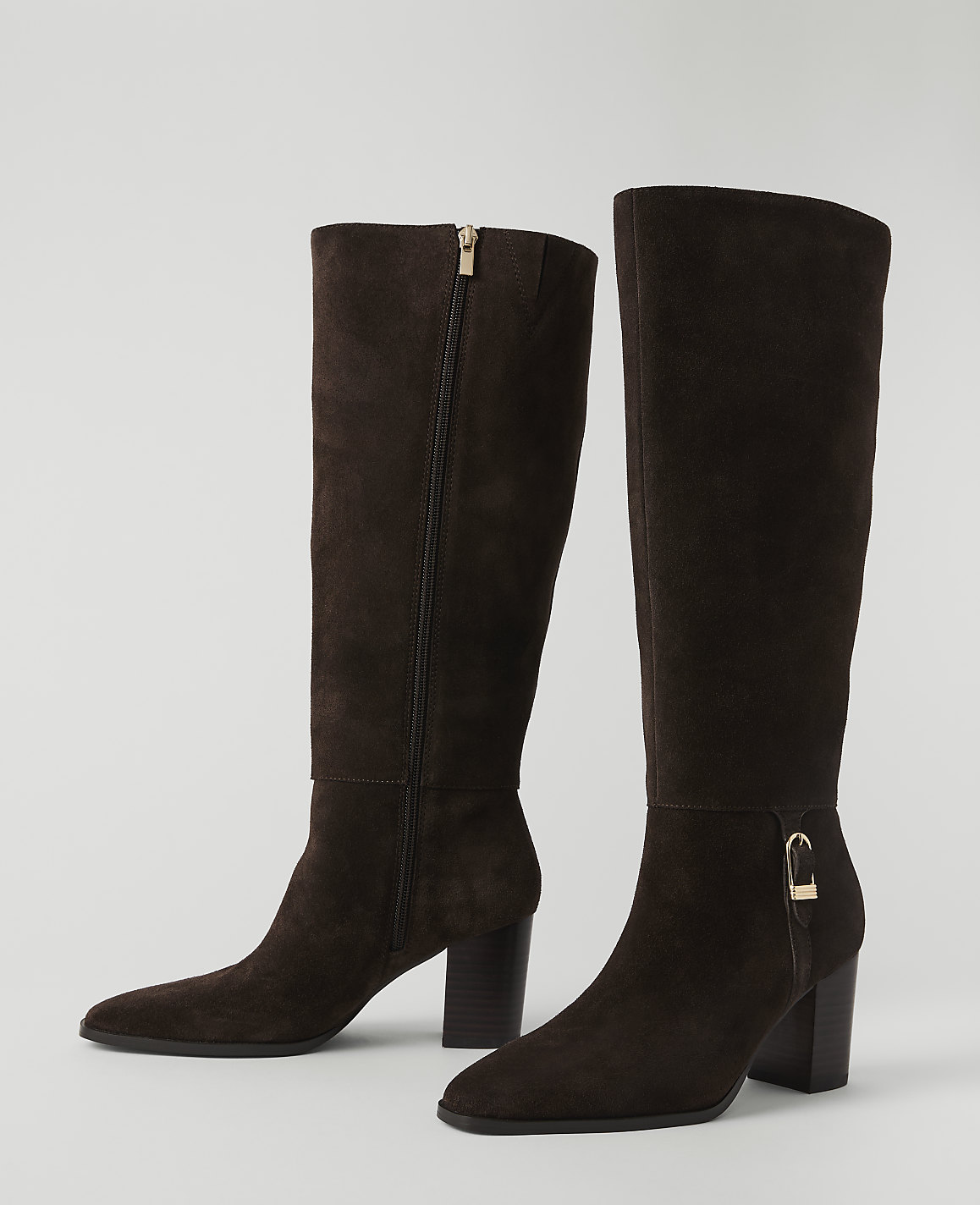 A pair of dark brown suede knee-high boots with gold accents stand on a plain white background.
