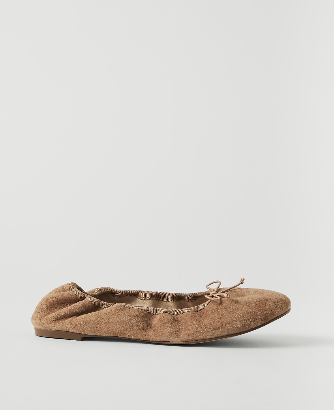 A tan suede ballet flat with a small bow sits on a plain white background.