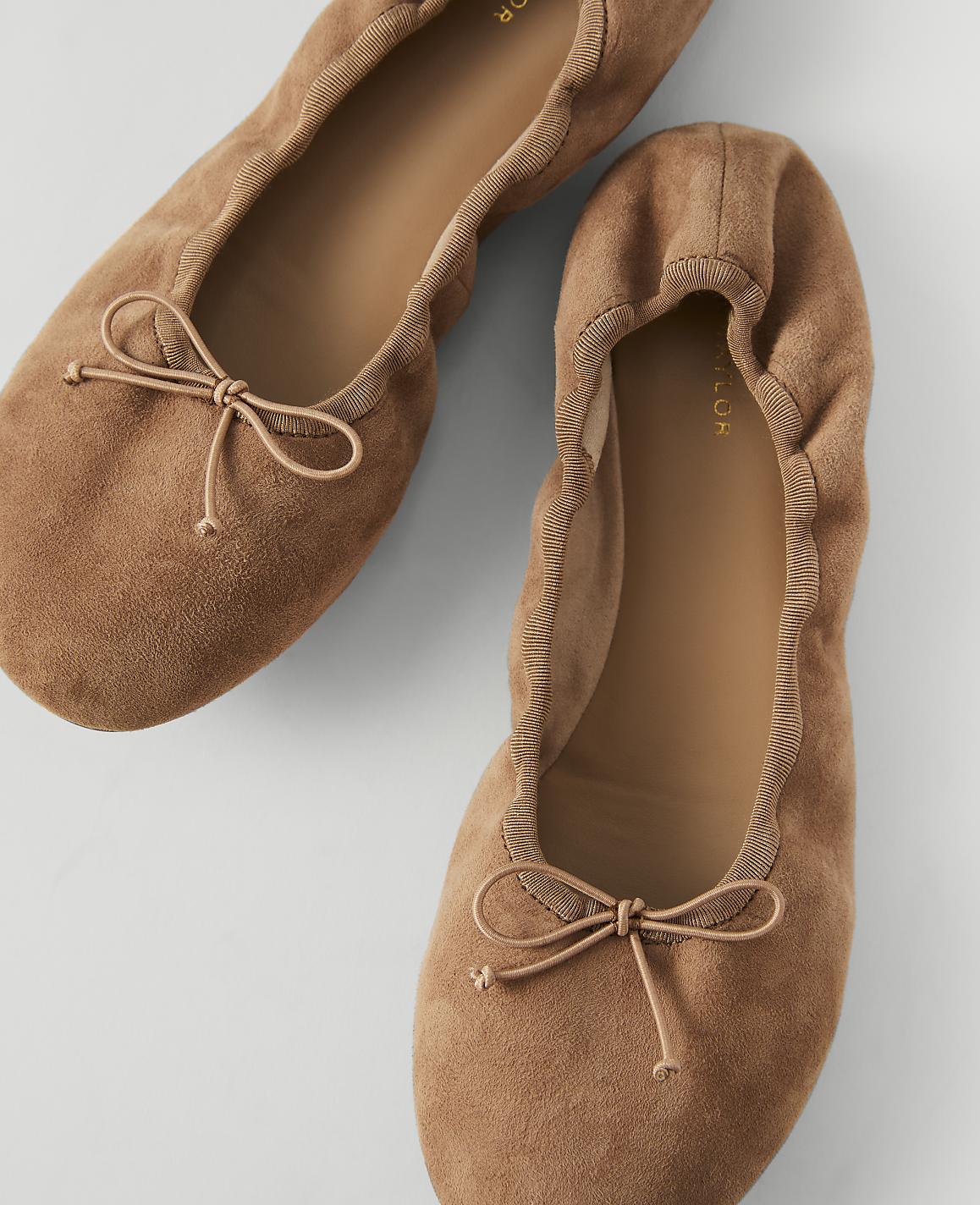 Two tan suede ballet flats with bows are arranged on a light gray background.