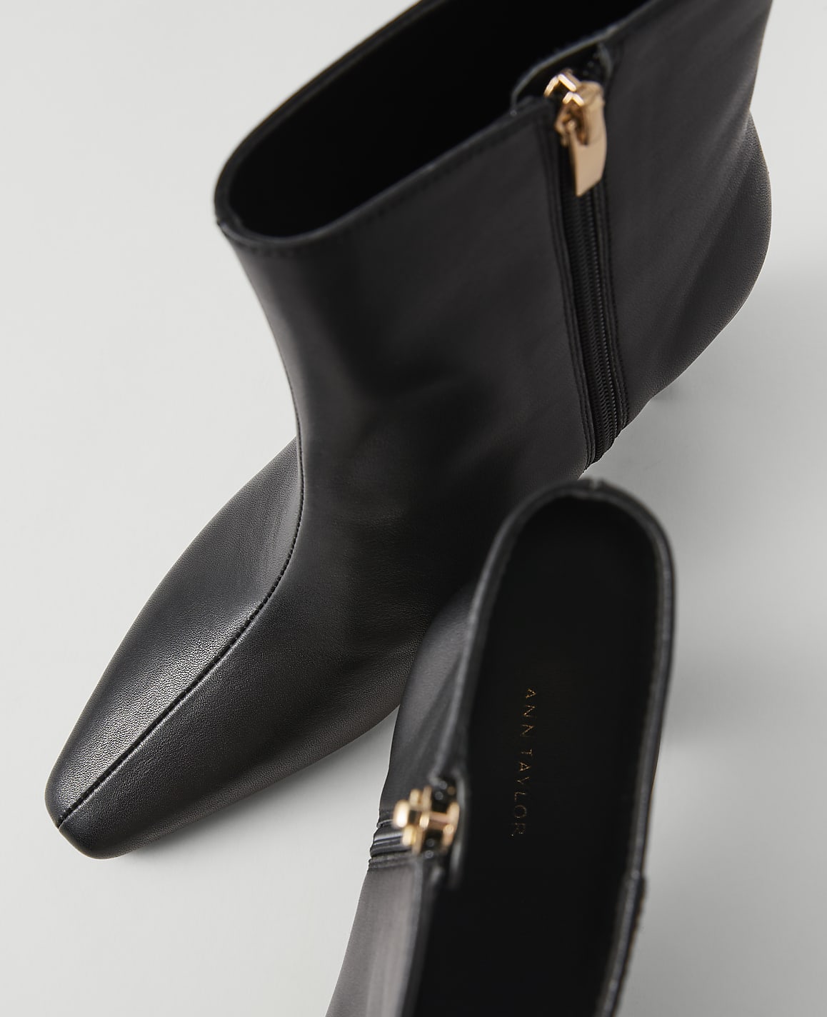 A pair of black leather ankle boots with gold zippers are displayed on a white background.