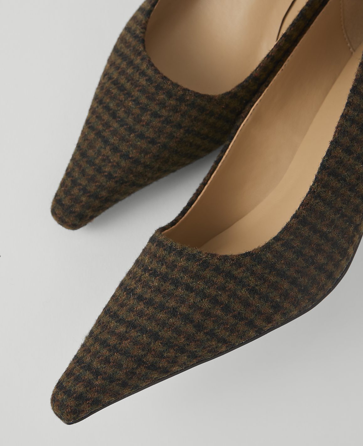A pair of brown houndstooth pointed-toe pumps rests on a plain white background.