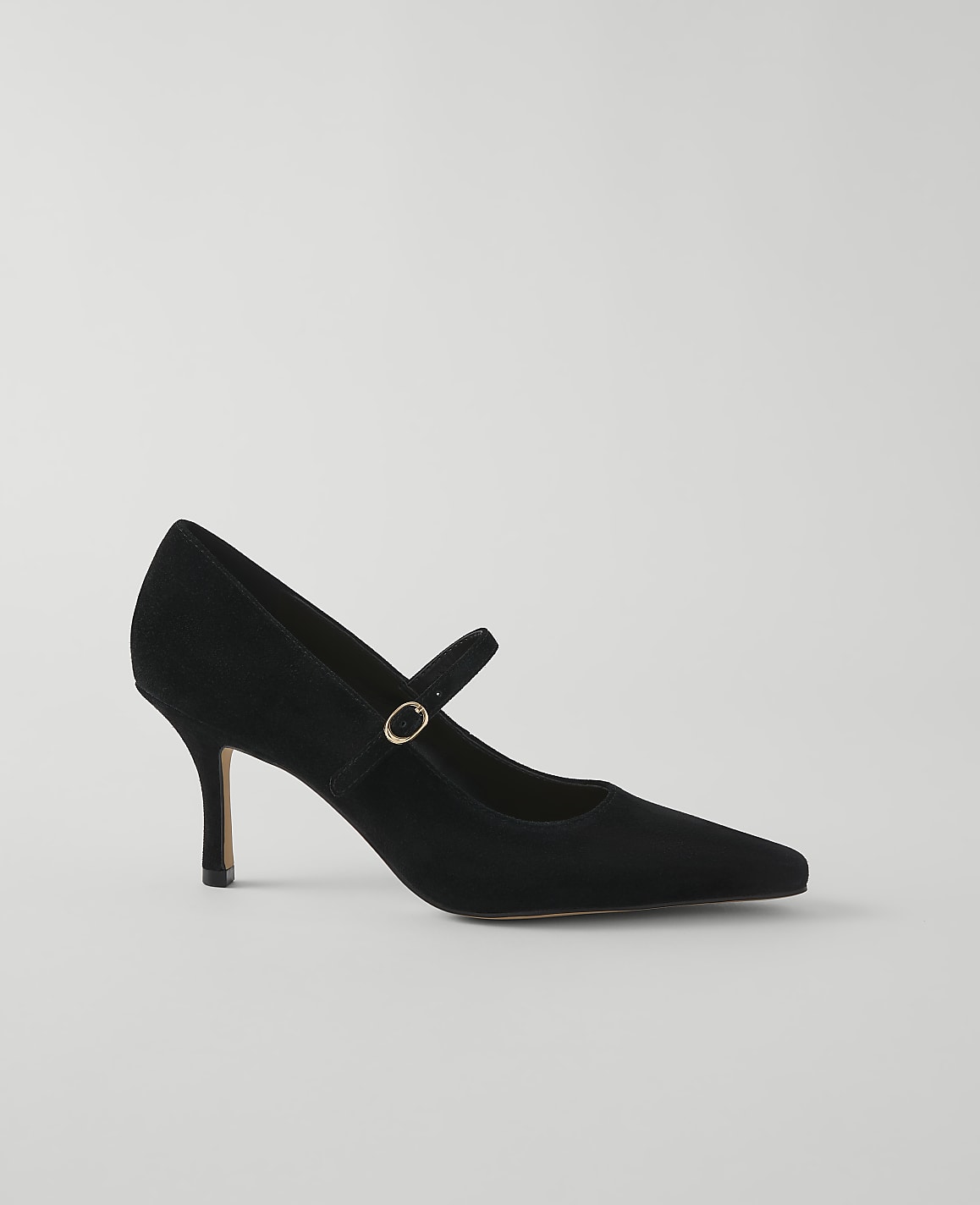 A black suede Mary Jane pump with a pointed toe and a thin heel rests on a plain, light gray background.