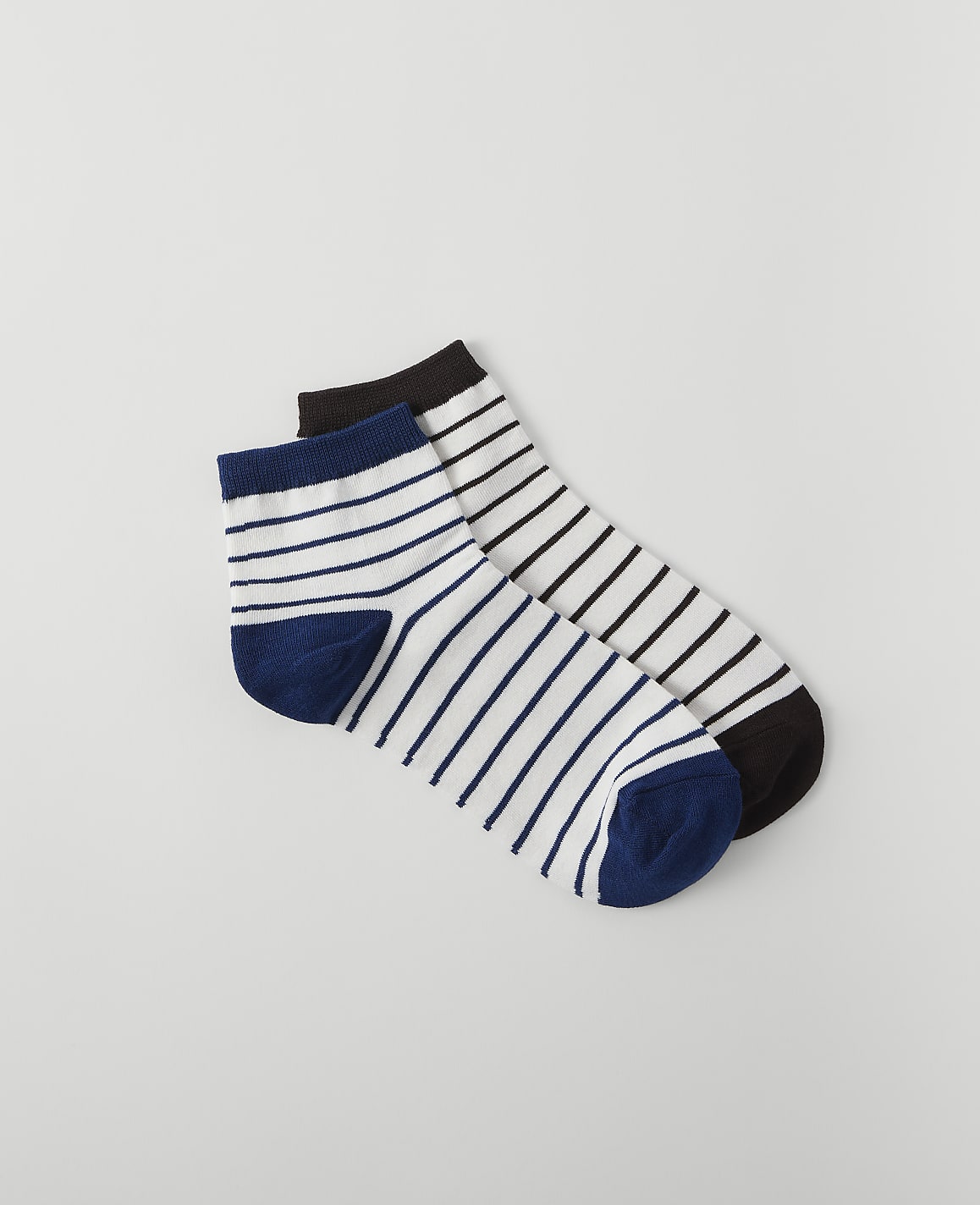 Two pairs of striped socks, one with blue and white stripes and the other with black and white stripes, lie on a plain white background.