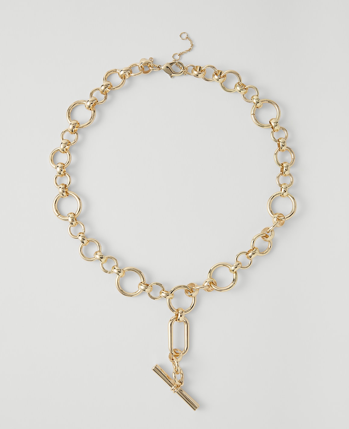 A gold chain necklace with a toggle clasp and pendant rests on a plain white background.