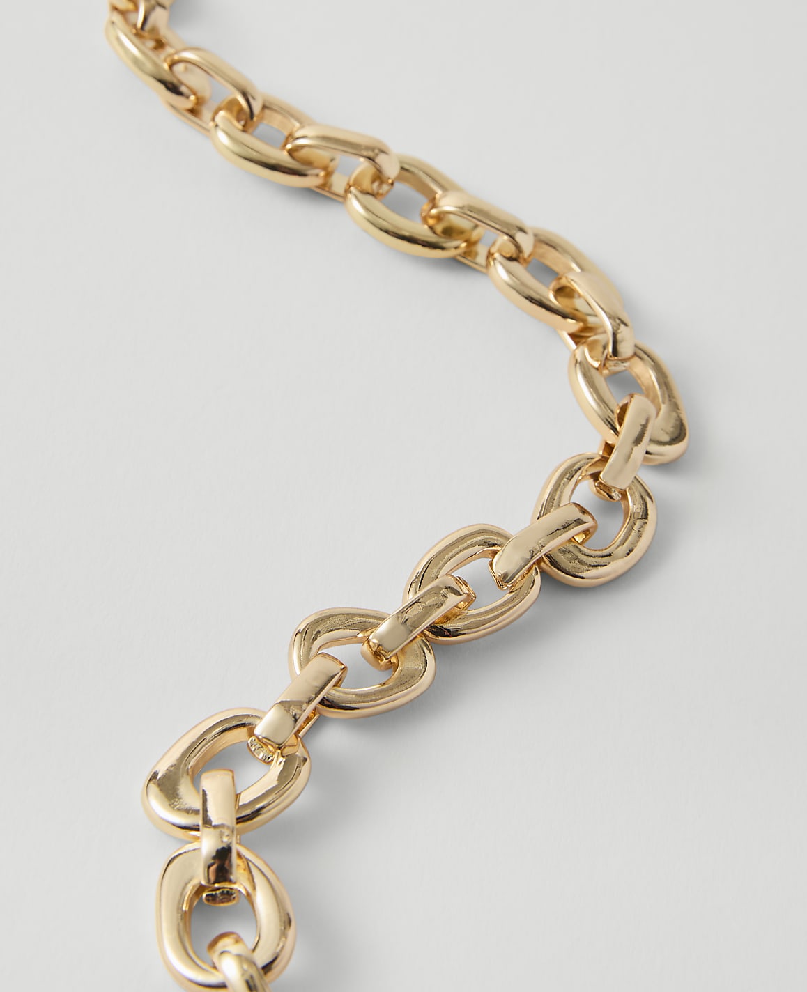 A close-up of a gold chain with oval links curves across a plain white background.