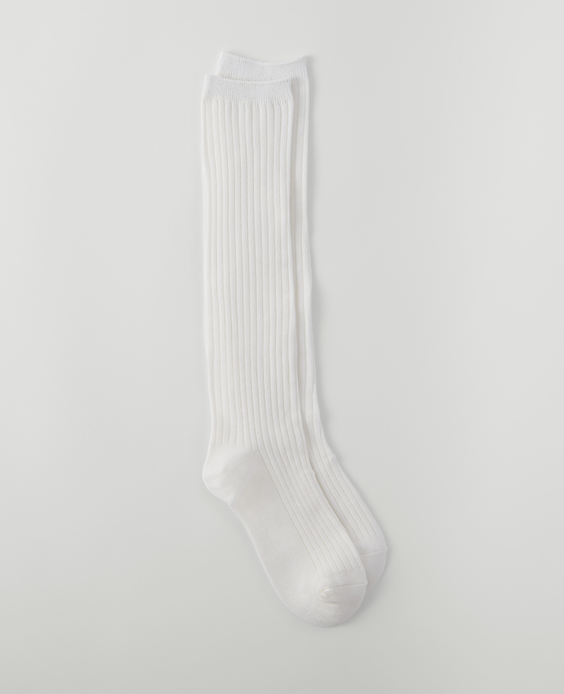 A pair of white ribbed knee-high socks lies on a plain white background.