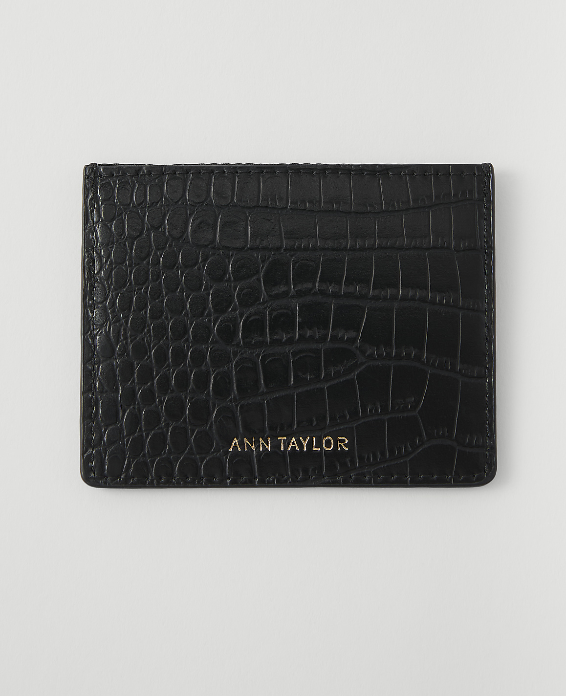 A black, crocodile-embossed cardholder with "ANN TAYLOR" in gold lettering rests on a plain white background.