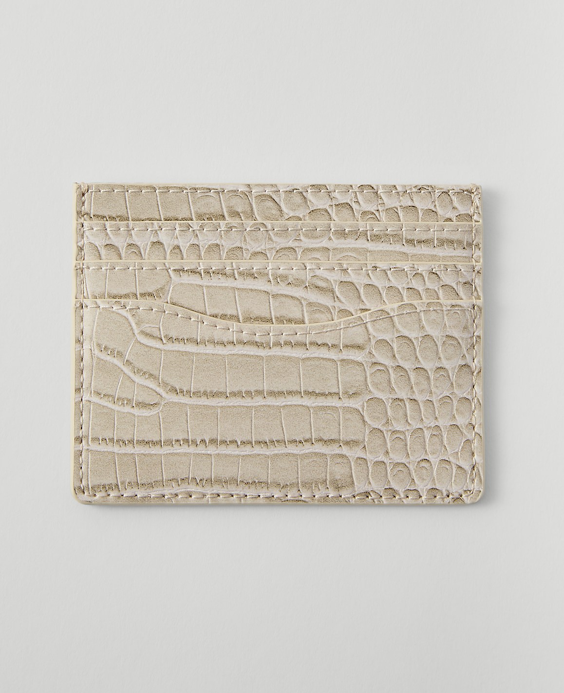 A light beige, crocodile-embossed cardholder with multiple slots rests on a plain white background.