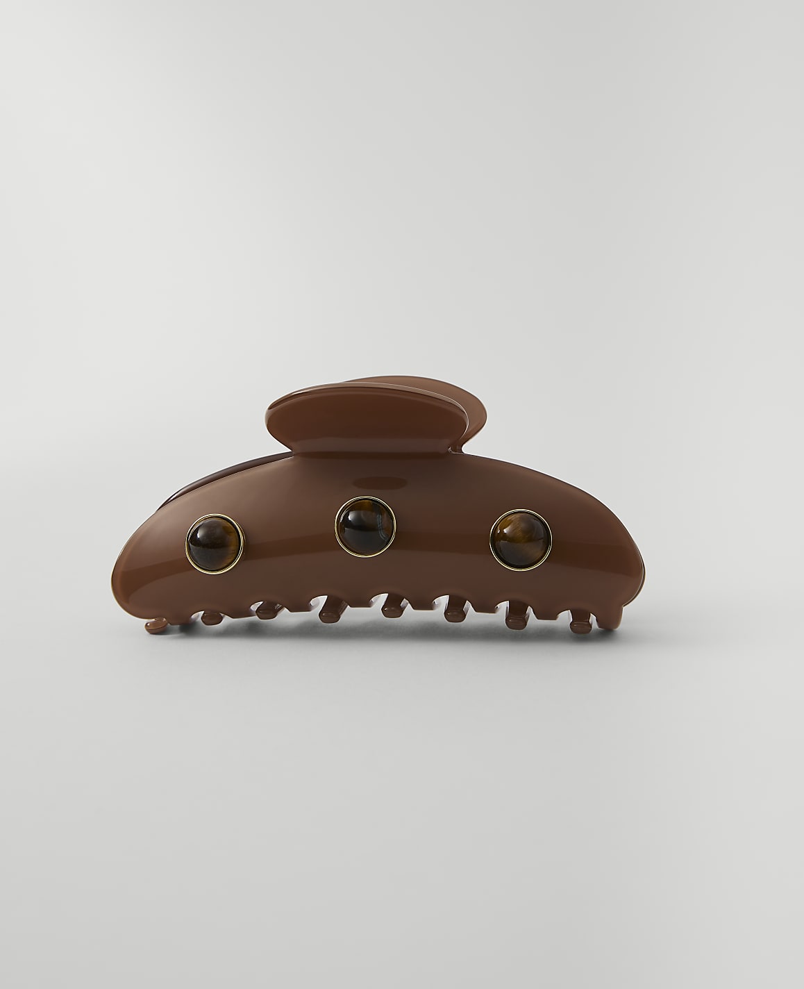 A brown claw clip with three amber-colored stones is centered against a plain, light gray background.