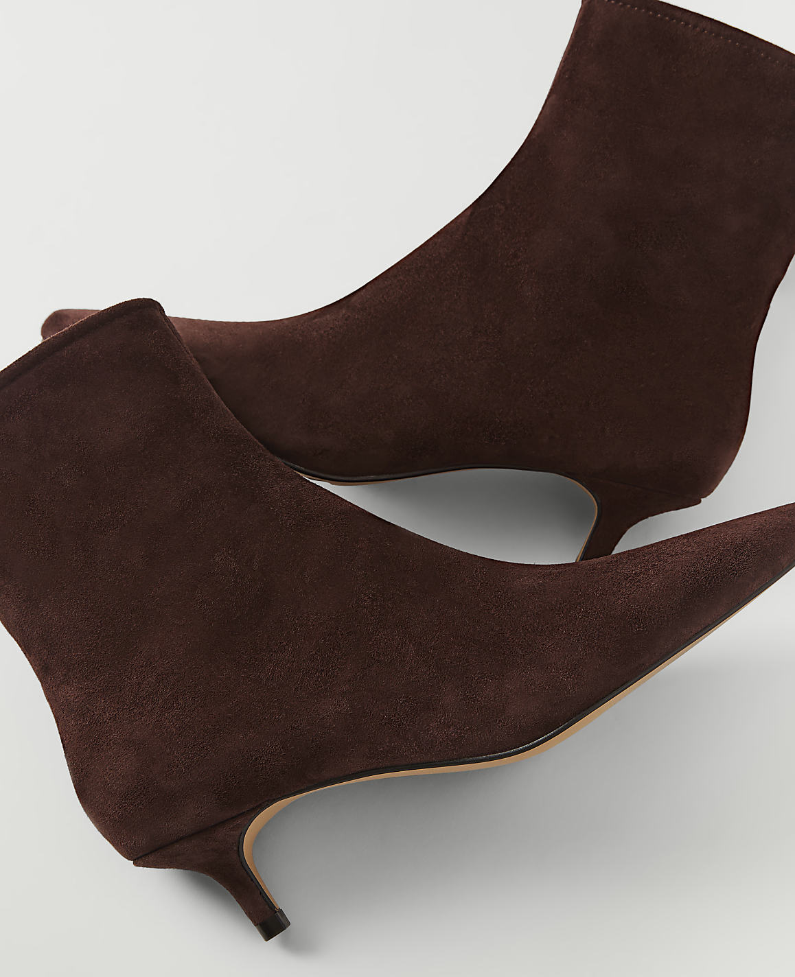 A pair of brown suede kitten heel ankle boots are displayed against a plain white background.